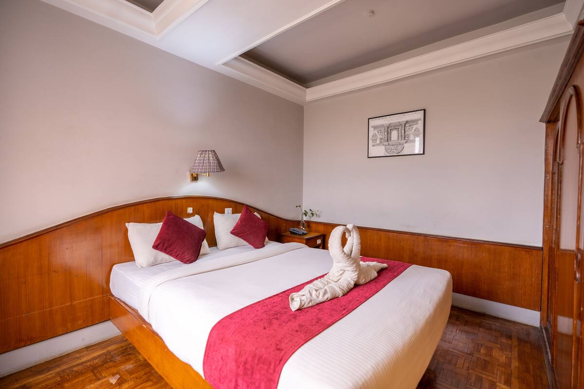 Een hotelkamer met een houten hoofdbord, een groot bed met wit en rood beddengoed, een rode plaid en een handdoek gevouwen in de vorm van een zwaan.