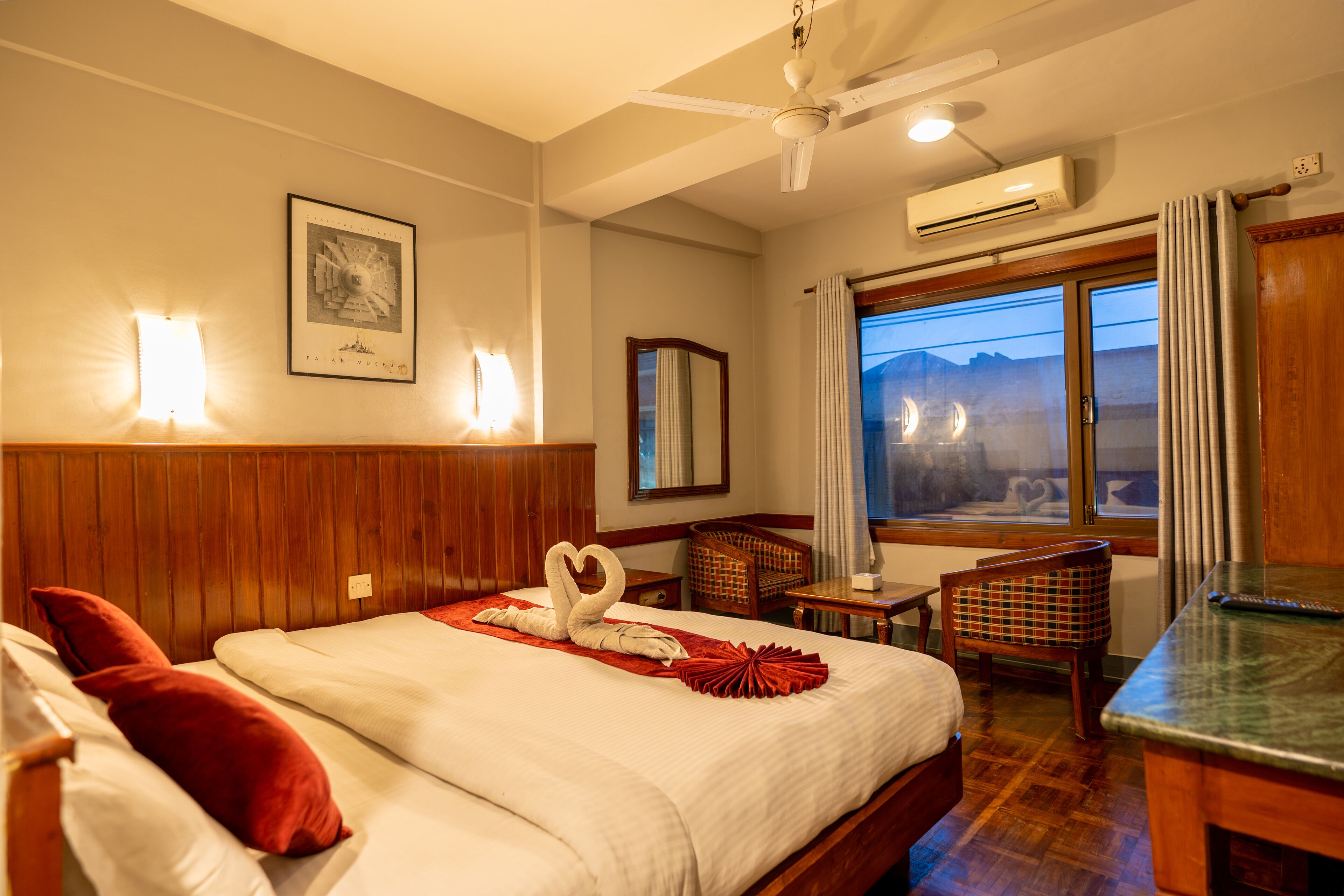 A hotel room with a bed, a desk, a chair, a window with a view, and an air conditioning unit.