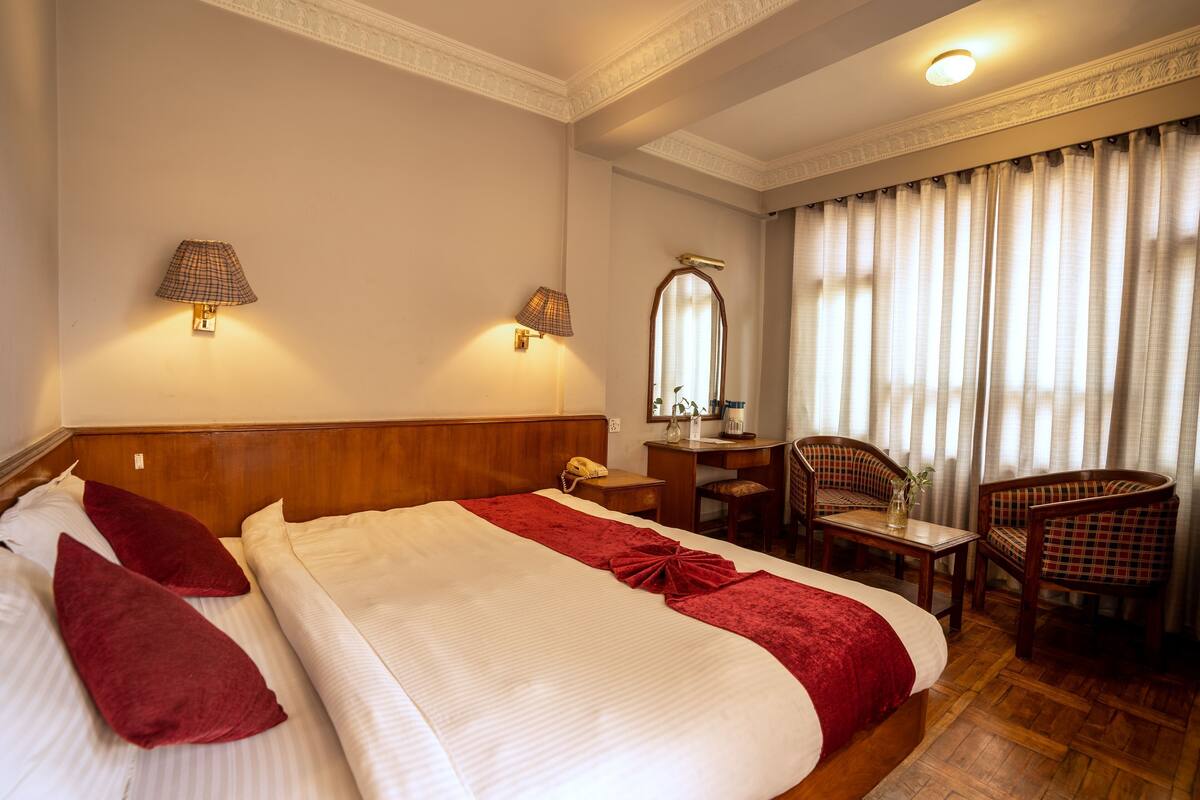 Een hotelkamer met een groot bed, twee bedlampen, een bureau met stoel, en een spiegel.
