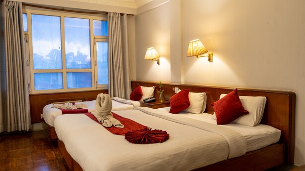 Quarto de hotel com duas camas, uma janela grande com cortinas e luminárias fixadas na parede.