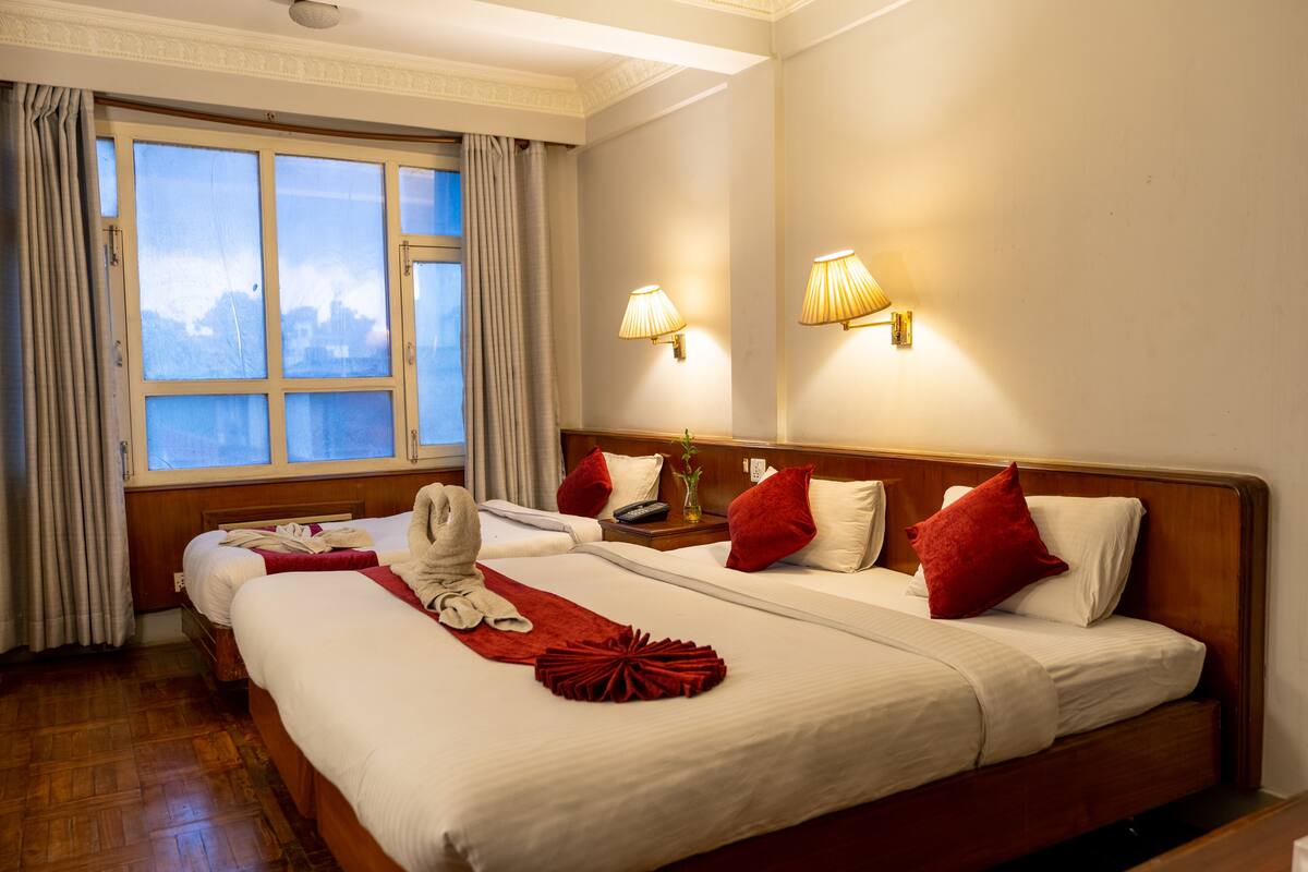 Een hotelkamer met twee bedden, een groot raam met gordijnen en wandlampen.