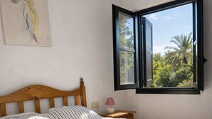 Ein Schlafzimmer mit Bett, Nachttisch, Lampe, einem Fenster mit geöffnetem Rollo und einem Bild an der Wand.