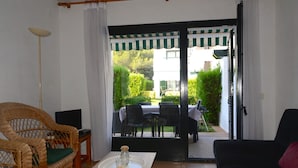 Ein Zimmer mit Korbmöbeln, einem Tisch mit Kerze und Blick auf eine Außenpatio mit Tisch und Stühlen.