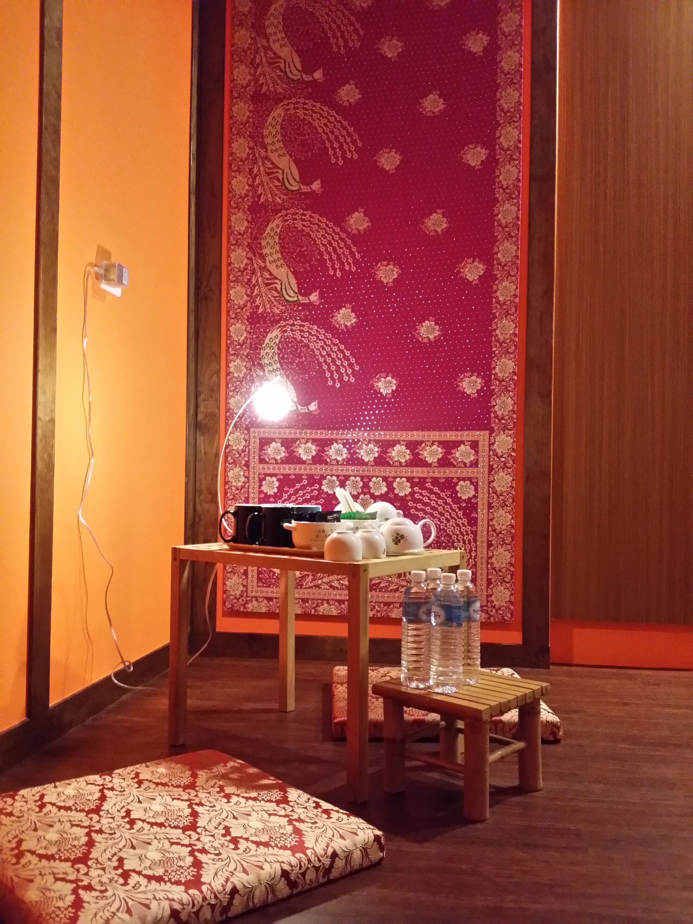 A room with a patterned wall, a table with kitchenware, a water dispenser, and a lamp.