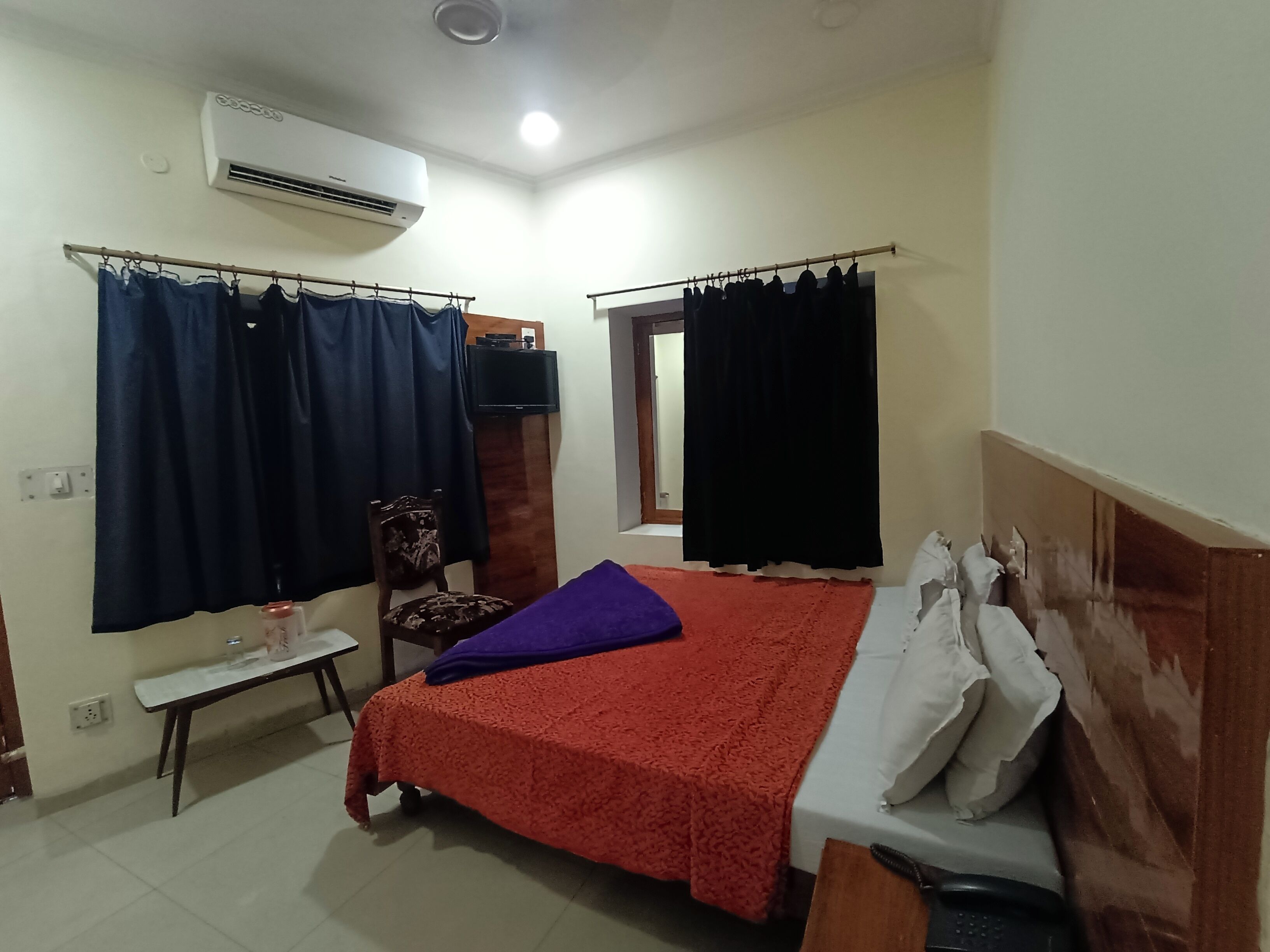 A bedroom with a bed, a chair, a small table, and an air conditioning unit.