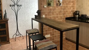 Eine Küche mit weißer Ziegelwand, Fliesenrückwand, einem Holztisch, zwei Hocker, einer Kaffeemaschine und einem Toaster.