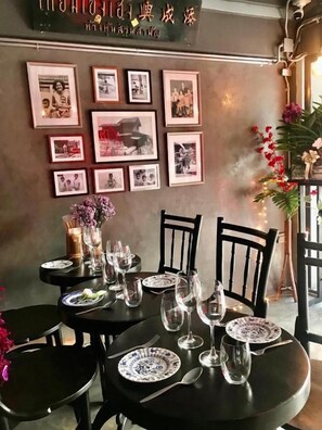 A restaurant interior with tables set for dining, framed pictures on the wall, and a decorative plant. - Tang House (Bangkok)