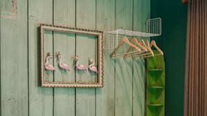 A room with a green cabinet, a framed picture of flamingos, a plant, and a hanging rack with clothes. - Tang House (Bangkok)