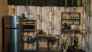 A compact kitchen with a stainless steel refrigerator, a microwave, a sink, and a shelf with kitchenware. - Tang House (Bangkok)