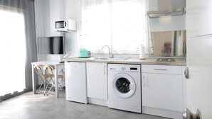 Een functionele keuken met een wasmachine, een magnetron en een spoelbak.