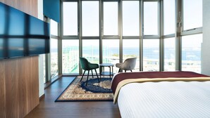 Una habitación de hotel moderna con un gran ventanal, una cama, dos sillas y una mesita.