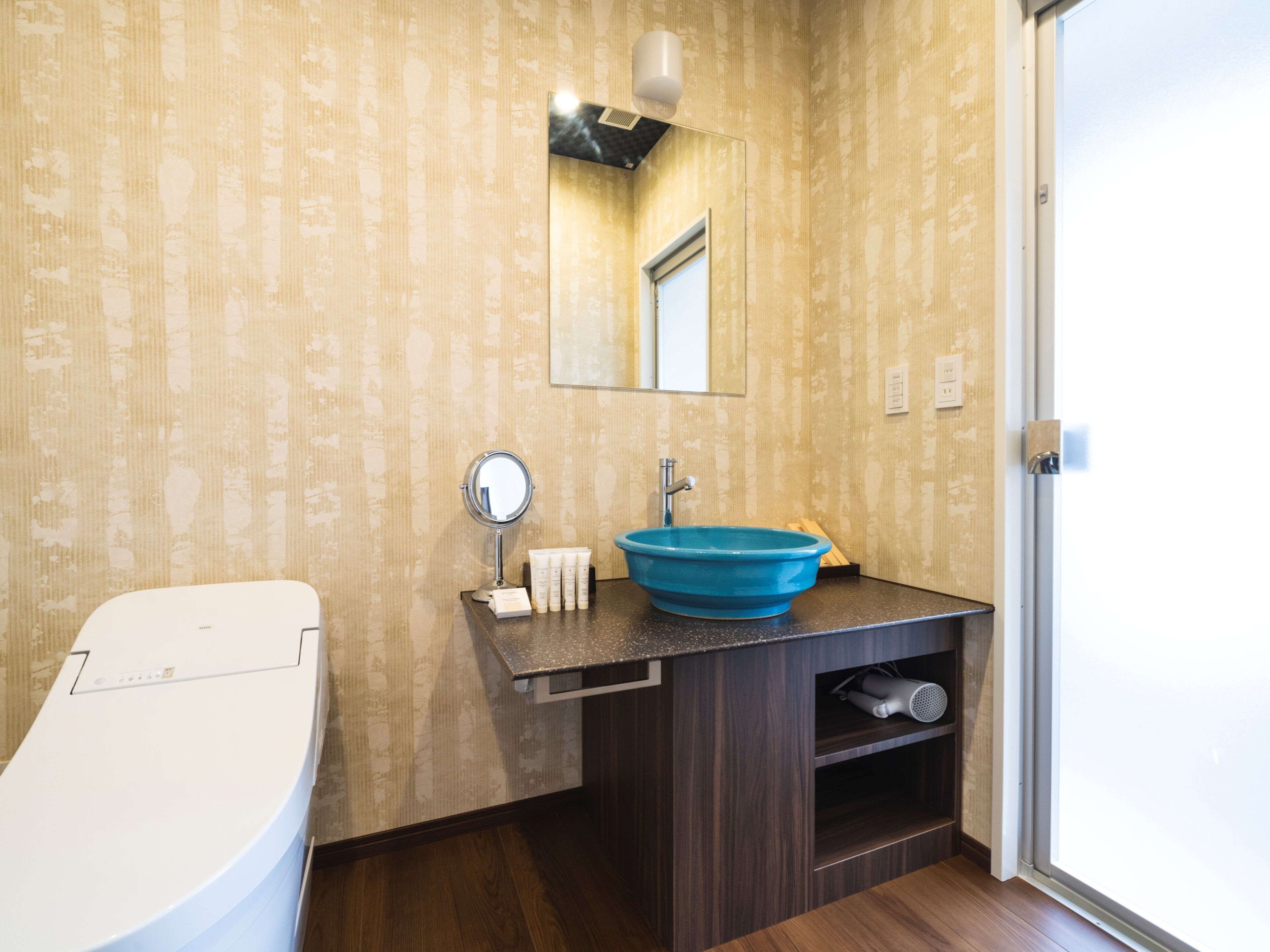 A bathroom with a white toilet, a blue sink, a mirror, and a wooden vanity.