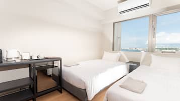 A hotel room with two beds, a desk with a coffee maker, and a large window offering a city view.