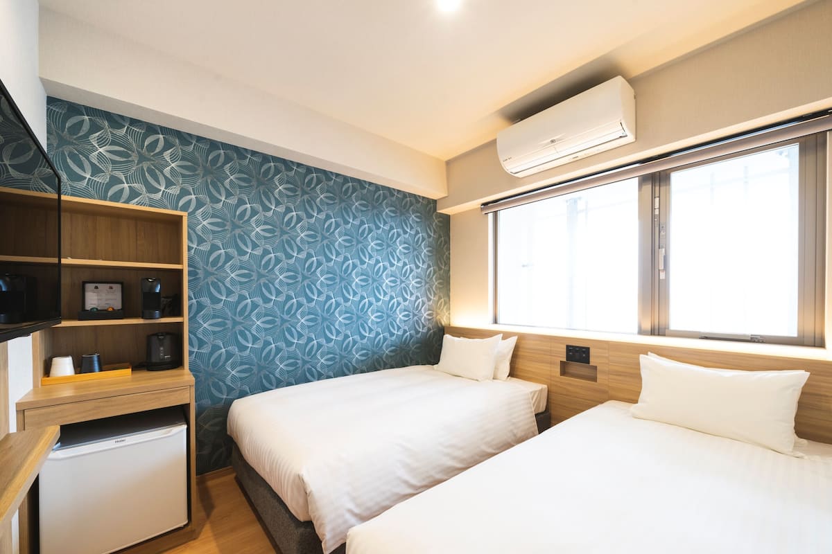 Quarto de hotel com duas camas, uma kitchenette pequena, aquecedor embutido e janela com vista.