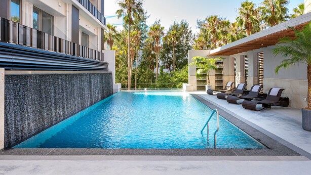 Una piscina con diseño moderno, rodeada de sillones de descanso y palmeras.