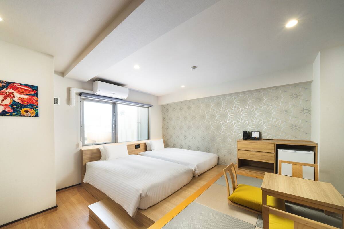 Quarto de hotel moderno com duas camas, uma escrivaninha, uma cadeira e uma mesinha.