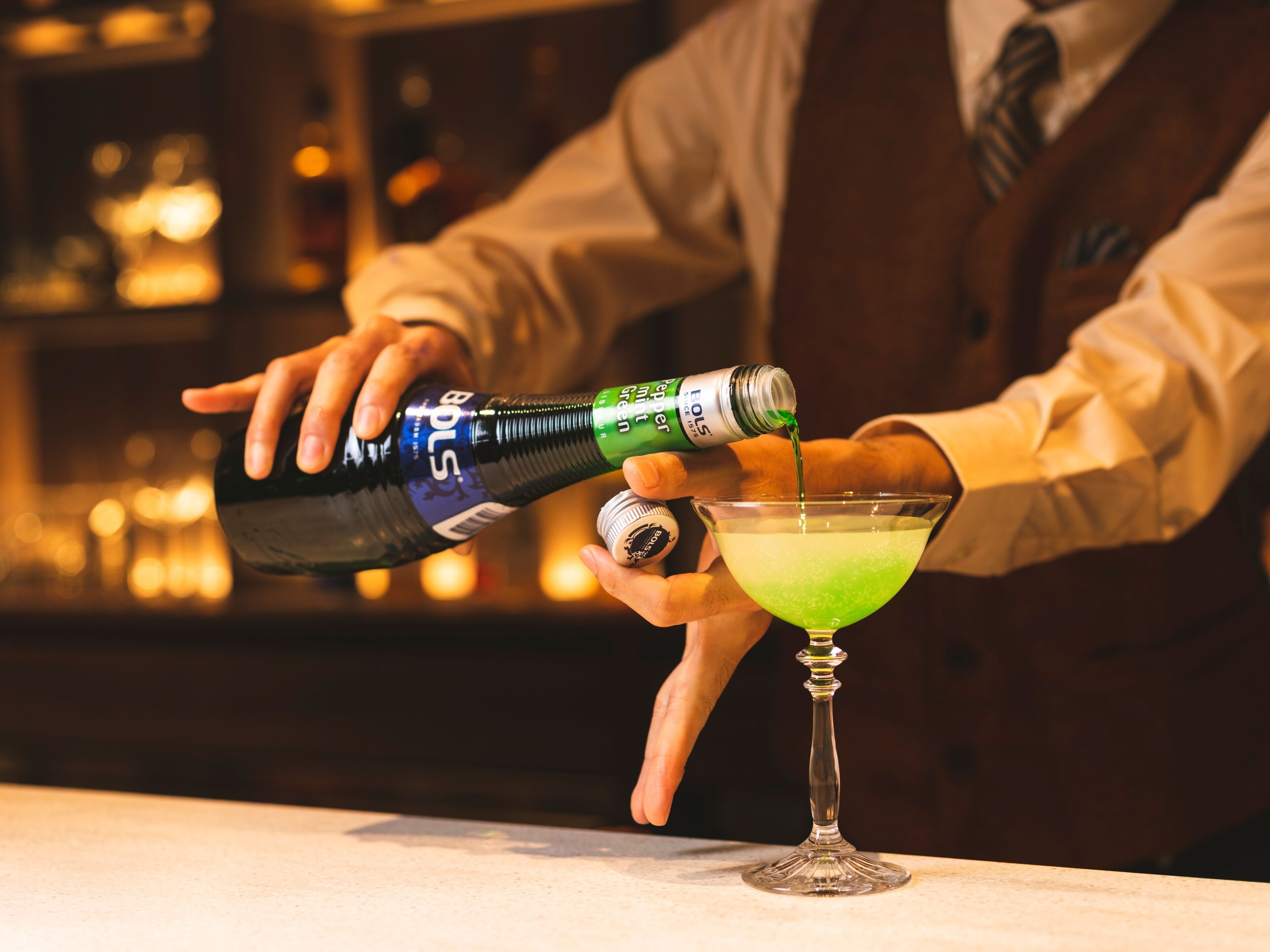 Um bartender servindo um líquido verde num copo de martini.