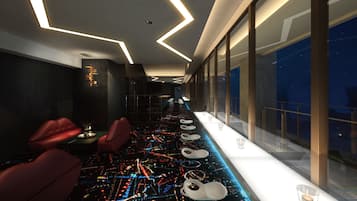 A modern hotel lobby with a long reception desk, seating area, and large windows offering a view of the night sky.