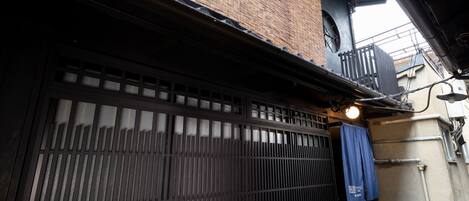 Edificio japonés tradicional con fachada de madera, puerta corredera negra y un pequeño balcón con una lámpara.