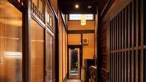 A corridor with traditional wooden doors and sliding glass doors, leading to a room with a bed and a nightstand. - Kanade Matsubaragokomachi (Kyoto)