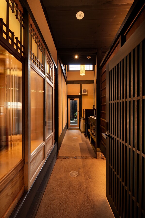 A corridor with traditional wooden doors and sliding glass doors, leading to a room with a bed and a nightstand.