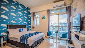 Ein Hotelzimmer mit Bett, Fernseher, Balkon mit Blick und einem Essbereich mit Stühlen.