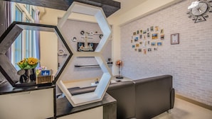 Ein Empfangsbereich mit modernem Design, mit einem geometrischen Spiegel, einer Rezeption und einer Wand mit gerahmten Bildern.