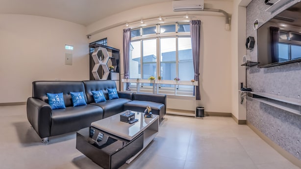 Ein modernes Wohnzimmer mit einem schwarzen Ledersofa, einem Glastisch und einem großen Fenster mit Vorhängen.