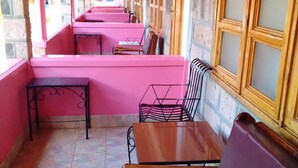 Un espace extérieur abrité, doté de tables et de bancs en bois, de murs en pierre et de grandes fenêtres.