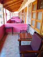 A covered outdoor seating area with wooden tables and benches, stone walls, and large windows.