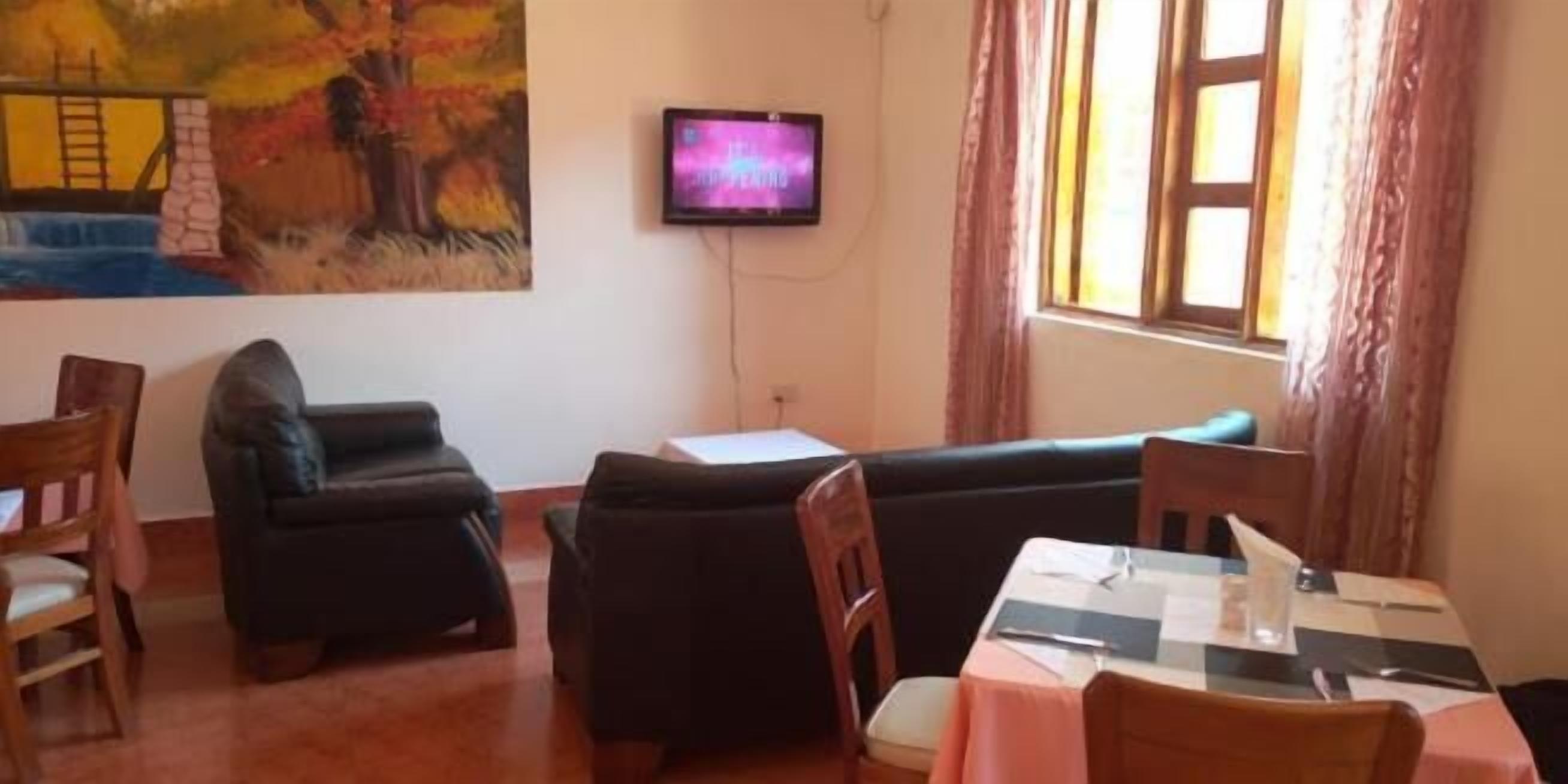 A room with a sofa, a dining table with chairs, a TV mounted on the wall, and a window with curtains.