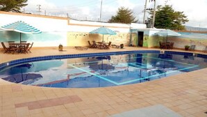 Une piscine avec un sol carrelé, des chaises longues et des parasols.