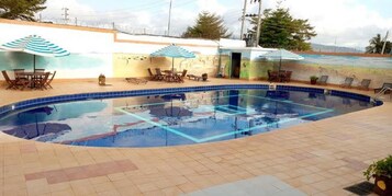 A swimming pool with tiled flooring, lounge chairs, and umbrellas.