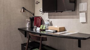 Un petit espace de travail fonctionnel, équipé d’un bureau, d’une chaise et d’un téléviseur à écran plat fixé au mur.