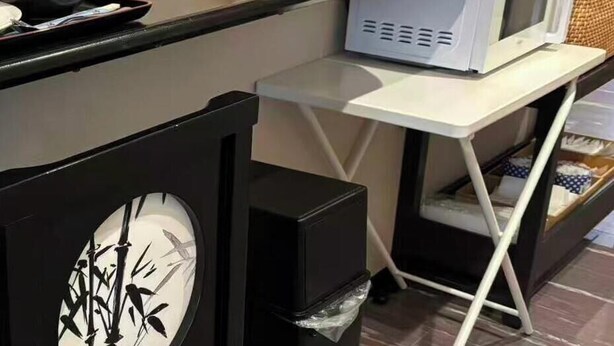Una kitchenette con microondas, un bote de basura y una mesita con una caja de pañuelos.