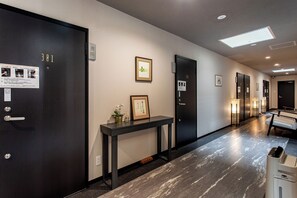 Pasillo de hotel con puertas de madera oscura, una recepción, obras de arte enmarcadas y una zona de estar con mesa y sillas.