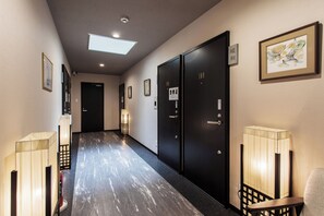 Un pasillo de hotel con puertas negras, piso de baldosas y lámparas en la pared.