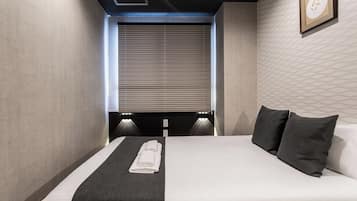 A hotel room with a bed, a window with blinds, a wall-mounted light, and a framed picture.