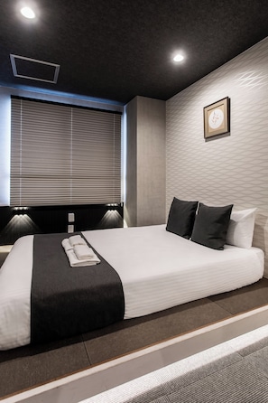 Habitación de hotel moderna con una cama grande, una ventana con persianas, un reloj de pared y un pequeño marco de fotos.