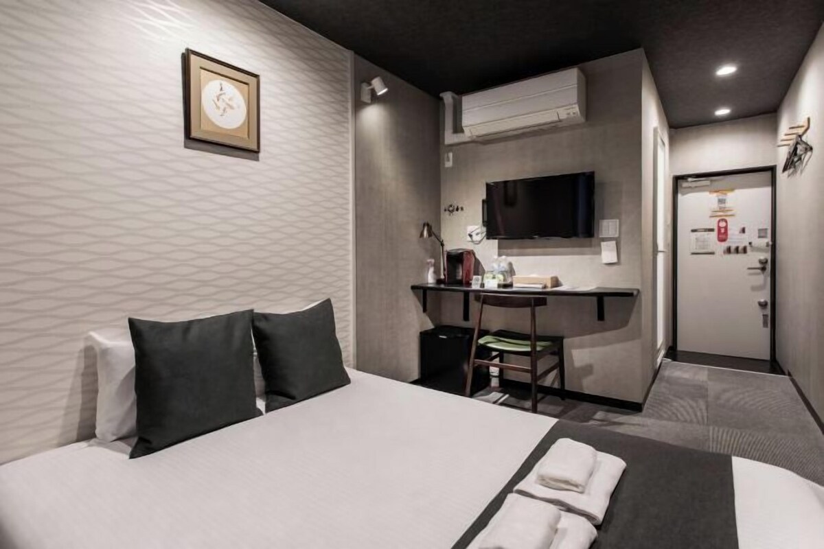 Ett hotellrum med en säng, ett skrivbord, en stol och en tv.
