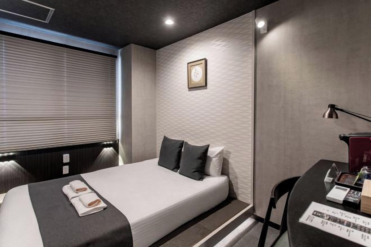 Ein Hotelzimmer mit einem Bett, einem Nachttisch, einer Lampe und einem Fenster mit Jalousien.