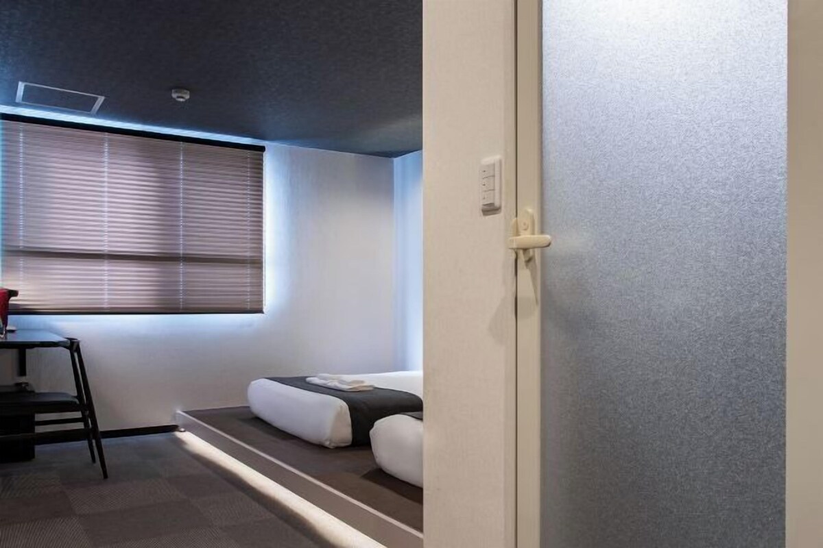 A small room with a bed, a desk, and a window with blinds.