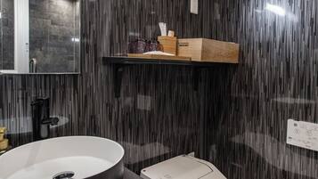 Un baño moderno con un lavamanos negro grande, un inodoro blanco y un estante de madera sobre el lavamanos.