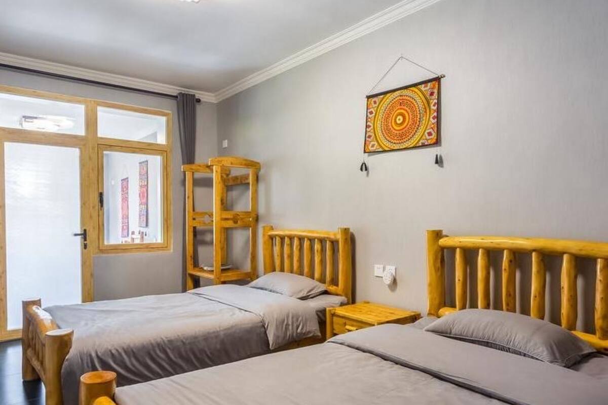 A room with two wooden beds, a wooden nightstand, a window with curtains, and a wall hanging.