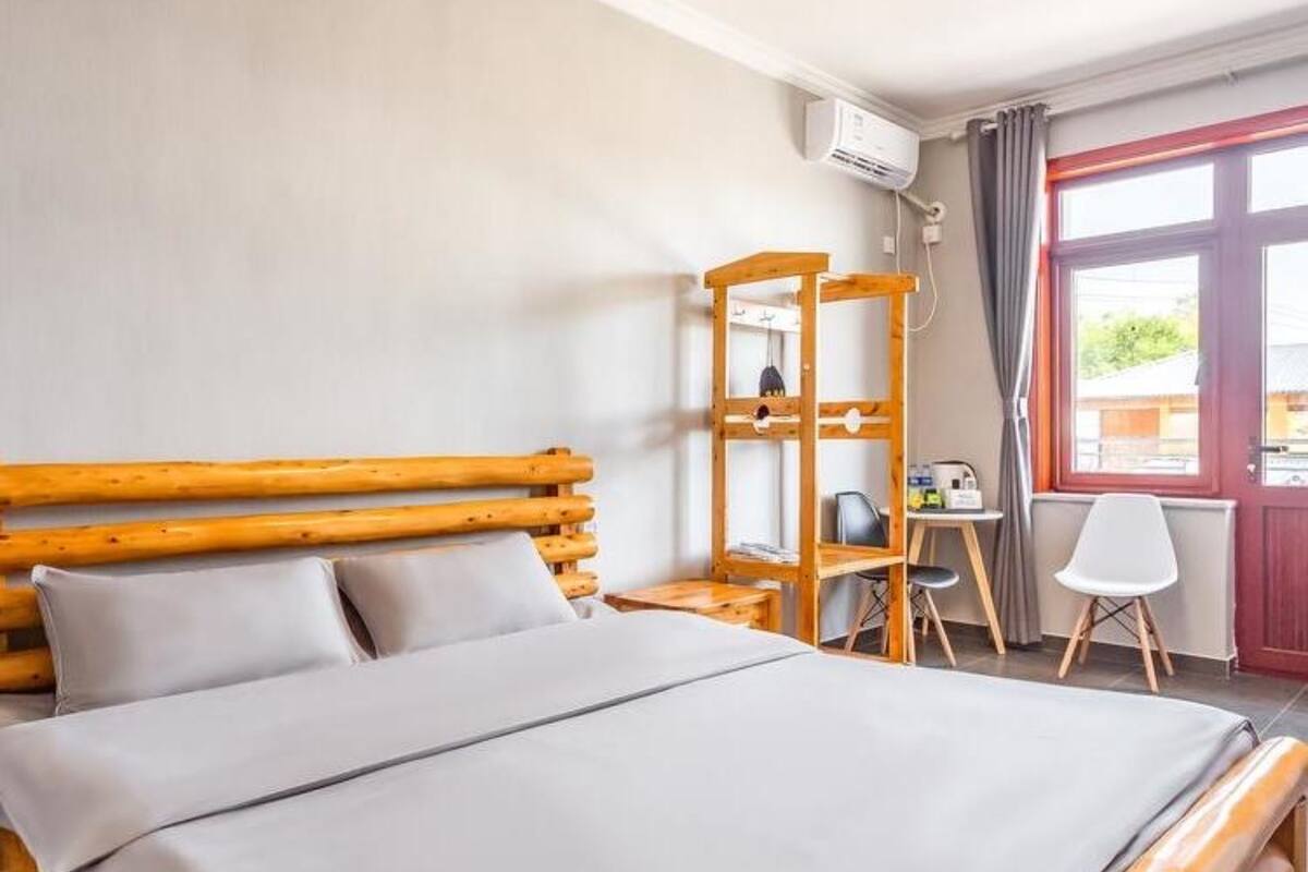 A bedroom with a wooden bed, a desk, a chair, and a window with curtains.