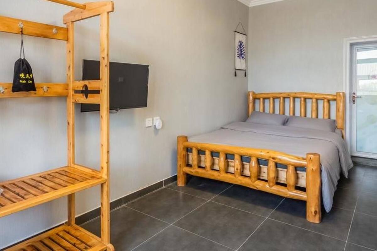 A room with a wooden bed, a TV mounted on the wall, and a wooden shelf unit.