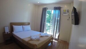 A hotel room with a bed, a nightstand, a TV, and a window with curtains. - Nathaniel Hotel (Daet)