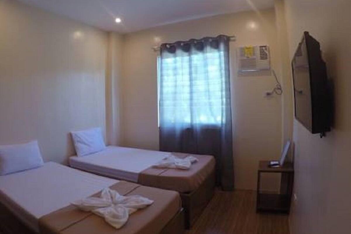 Una habitación de hotel con dos camas individuales, una mesita, un televisor y un ventanal con cortinas.