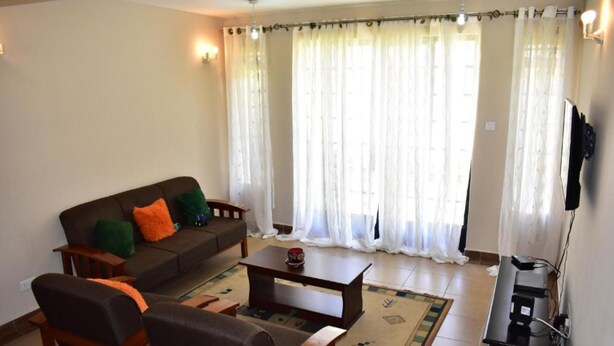 A living room with a sofa, chairs, a coffee table, and a TV stand. - Valbras Homestay Nairobi (Syokimau)