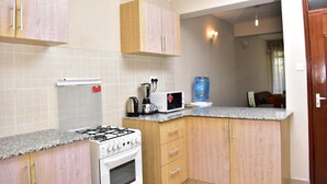 A compact kitchen with a gas stove, a microwave, and a water dispenser on the countertop. - Valbras Homestay Nairobi (Syokimau)